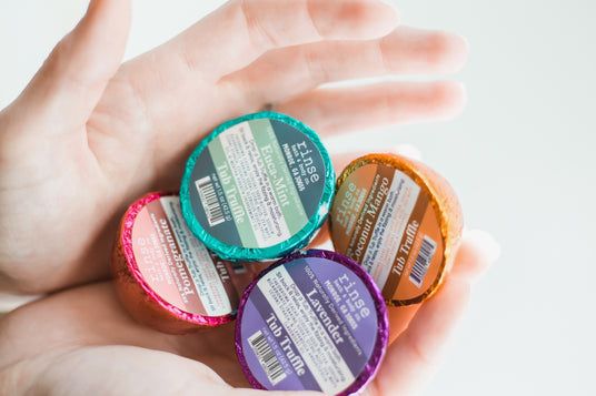Hands holding an assortment of colorful Rinse Tub Truffle bath bombs
