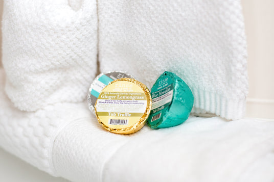 Gold and teal Rinse Tub Truffle bath bombs resting on a white knit blanket