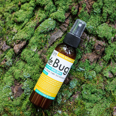 DeBug natural bug repellent spray resting on a mossy log in the forest